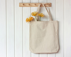 light rag bag with flowers hangs on a white wooden wall.