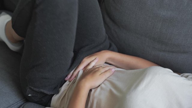 Woman with abdomen pain laying on the grey sofa. Painful periods. Digestive system problems.