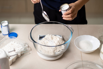 Woman adding bicarbonate soda to flour on a small kitchen scale while making cookies in the kitchen - obrazy, fototapety, plakaty