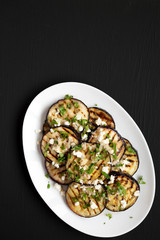 Homemade Grilled Eggplant with Feta and Herbs on a white plate on a black background, top view. Flat lay, overhead, from above. Copy space.