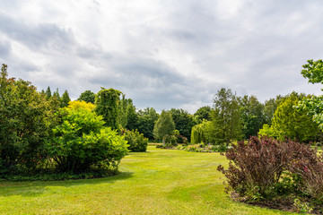 Between the threatening clouds a dim sun illuminates this beautifully landscaped garden with a great diversity of trees and flowering shrubs near the village of Harkstede in Groningen
