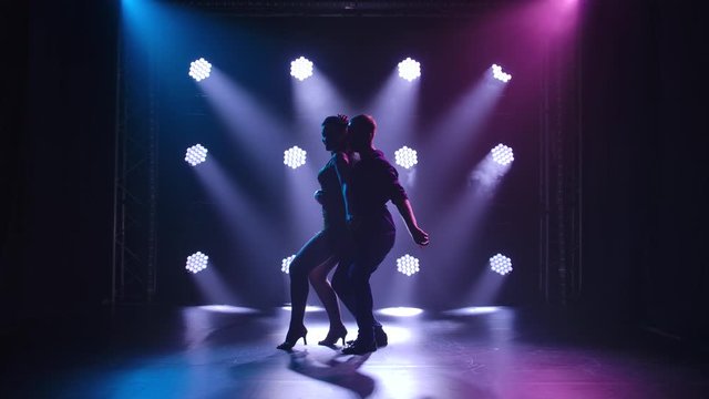 Young couple dancing latin music. Bachata, merengue, salsa. Shot in a dark studio with neon lights in the background.