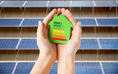 sustainability and consumption concept - close up of hands holding house with energy efficiency...