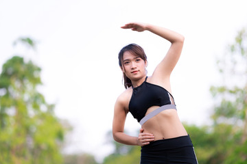 Active female raising left arms while standing during fitness or yoga practice. One young woman practicing yoga outdoors in garden. Healthy life and natural balance between body and mental development