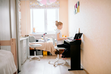 Pretty young musician playing classic digital piano at home during online class at home, social distance during quarantine, self-isolation, online education concept
