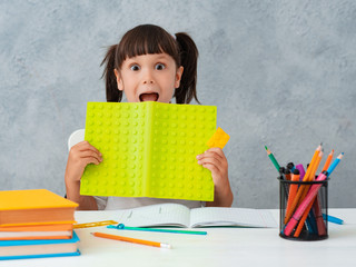 Back to school. Cute child schoolgirl sitting at a Desk in the room. The kid is learning and doing his homework. The girl is emotionally happy with her hands up