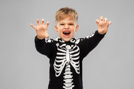 halloween, holiday and childhood concept - boy in black costume with skeleton bones making spooky faces over grey background