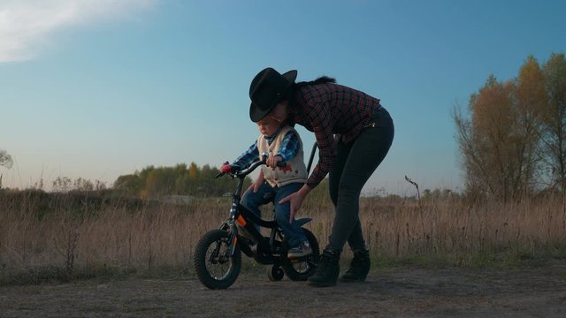 Mother Teaching Son To Ride Children Bike First Time on Countryside Rural Dirt Road. Slow motion