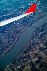 Airplane wing and aerial view during flight with ground area and river.