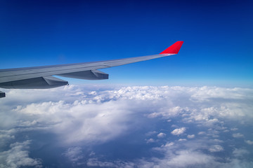 Airplane wing and aerial view during flight with clear blue sky and clouds