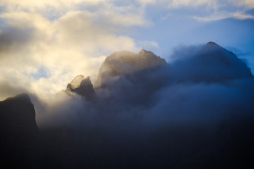Clouds swirling around high mountain peaks at sunrise.
