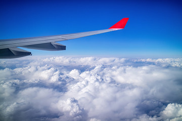 Airplane wing and aerial view during flight with clear blue sky and clouds