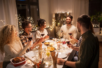 holidays, celebration and people concept - happy friends having christmas dinner at home drinking non-alcoholic red wine