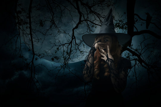 Scary halloween witch standing over dead tree, crow, birds, full moon and spooky cloudy sky, Halloween mystery concept