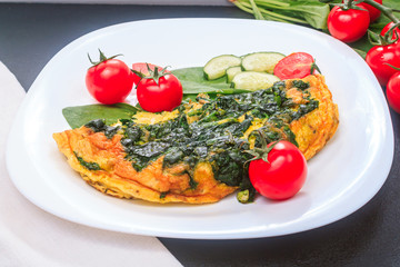 fried eggs with spinach and tomatoes, cucumbers on a white large plate on a black embossed table. top view, copy space, close up