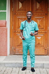 Fototapeta na wymiar Portrait of African male doctor with stethoscope wearing green coat with mobile phone at hand.