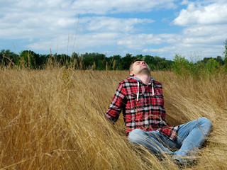 Naklejka na ściany i meble A young guy is sitting in the autumn grass. Relaxation and tourism in nature.