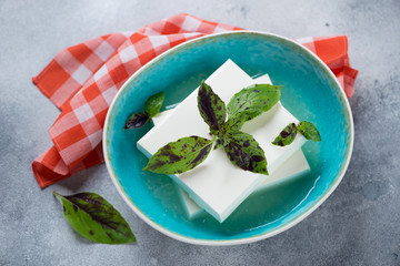 Turquoise bowl with blocks of brined feta cheese and fresh green basil, elevated view on a...