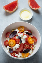 White bowl with grapefruit, feta cheese and cherry tomatoes salad, studio shot on a light-blue stone background