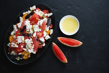 Grapefruit, feta cheese and tomato salad over black stone background, horizontal shot with copyspace, top view