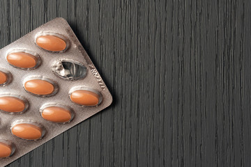 Brown pills in a silver blister pack on a dark wooden gray texture