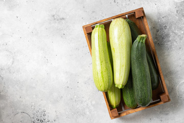 Raw zucchini. Zucchini in a wooden box on a light gray table. Top view with space for text. Zucchini crop