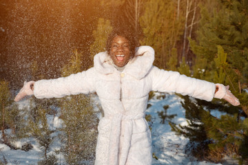 Fototapeta na wymiar Beautiful dark-skinned woman in a white fur coat throws snow sunlight.