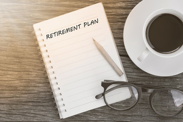 Fototapeta na wymiar Retirement plan word on notebook with glasses, pencil and coffee cup on wooden table. Retirement plan concept.