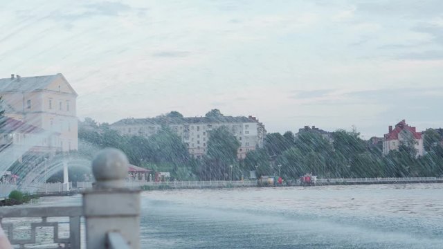 Landscape, ponds, parks, summer recreation concept - multi-colored fountains with illumination in form of arc falling from shore into large lake in evening before sunset in park area of city near port