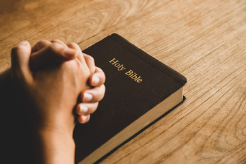 Women praying, Hands clasped together on her Bible in the whiteness over wooden table.