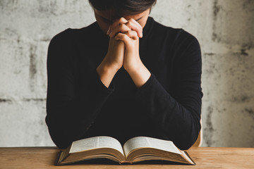 Women praying, Hands clasped together on her Bible in the whiteness over wooden table.