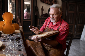 Focused senior carpenter peacefully working in his old-fashion workshop on new project. Carving and...