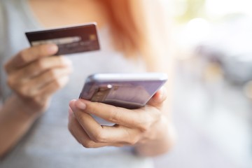 Close up of woman hands holding smart phone and and using cell credit card for online shopping payment.