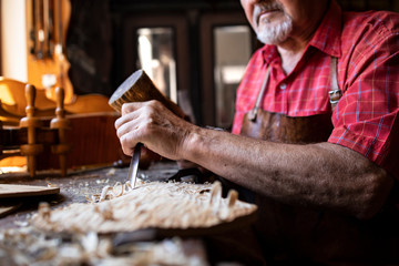 Fototapeta premium An experienced senior carpenter holding knife and hammer carving wooden board in his woodworking workshop.