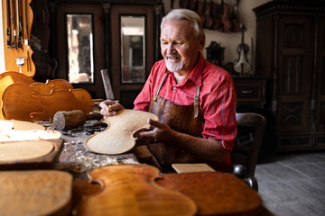 Professional senior carpenter making high quality violin instrument for students of music academy....
