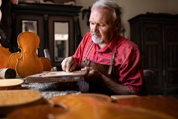 Senior carpenter craftsman carefully carving and shaping wood in his woodworking workshop. Creative...