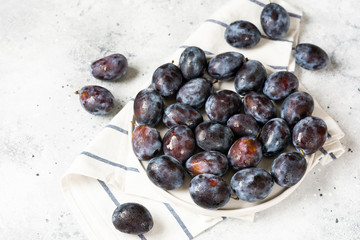 Ripe plum. A lot of plums in a white ceramic plate on a light gray table. Blue plums on a plate.  Healthy fruits	