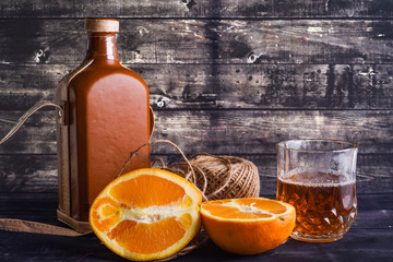 Bottle of whiskey and glass and ripe orange on a dark wood background. Glass of whiskey.