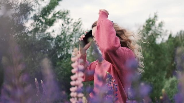 Pretty young happy woman in headphones dancing in a field of purple flowers