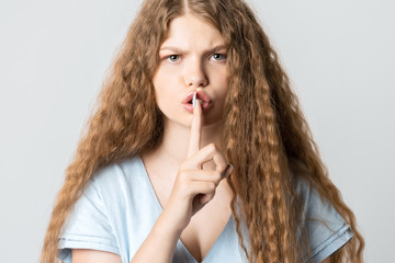 Emotional young woman with curly long hair keeping index finger at her lips, saying Shh, Keep silent, It's secret