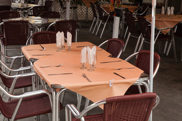 Empty restaurant terrace seats and tables prepared with glasses, napkins and dishware. Prepared for the service concept.