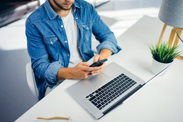 Young man with smartphone in his hands. Modern businessman at sunny office. Freelancer at work.