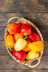 Sweet pepper. Red, yellow and orange peppers in a basket on a brown wooden table. Paprika close-up. Top view with space for text	