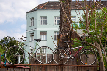 Zwei Fahrräder hängen an einem Zaun vor einer Häuserfassade