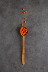 Wooden spoon with sea-buckthorn berries at gray textured background.