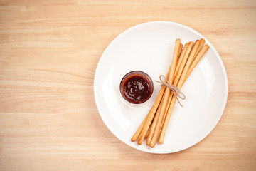 pack of breadsticks with ketchup dipping sauce in white dish on wood table