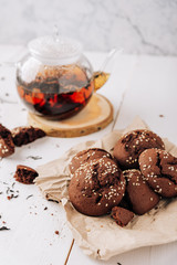 Teapot with black tea and homemade chocolate cookies on a white natural wooden background