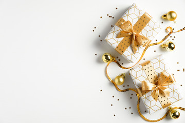 Holiday Christmas banner. Xmas background with luxury gift boxes, bright gold ribbon, glitter confetti stars, golden balls on white table. Flat lay, top view.