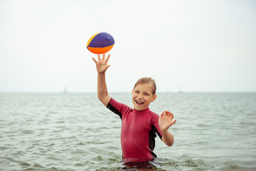 Happy teen girl in neoprene swimingsuit  playing with ball and running in sea