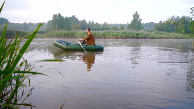 young stylish hipster fisherman sails in a boat on a lake or river between the reeds. A young man paddles on an inflatable boat. Relaxes in nature. camping by the water. Recreation